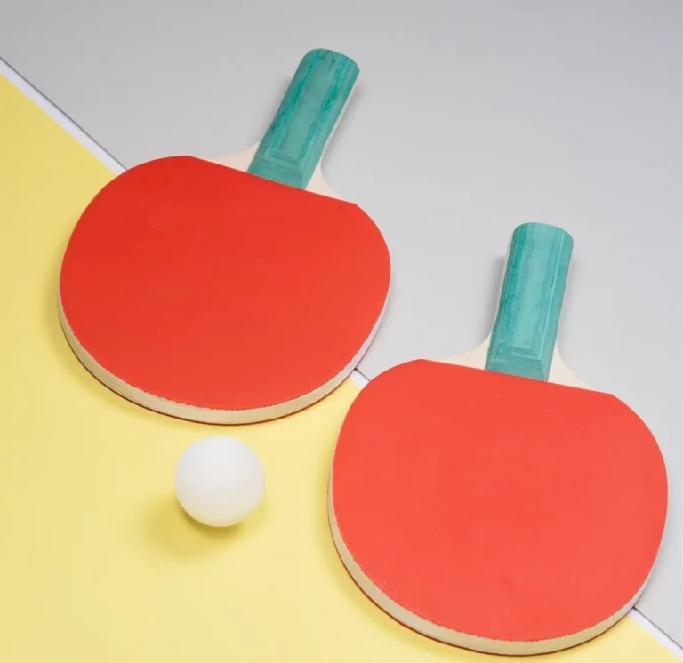 Deux raquettes de ping pong avec un revêtement rouge, posées côte à côte, légèrement décalées, avec une balle de tennis de table entre elles